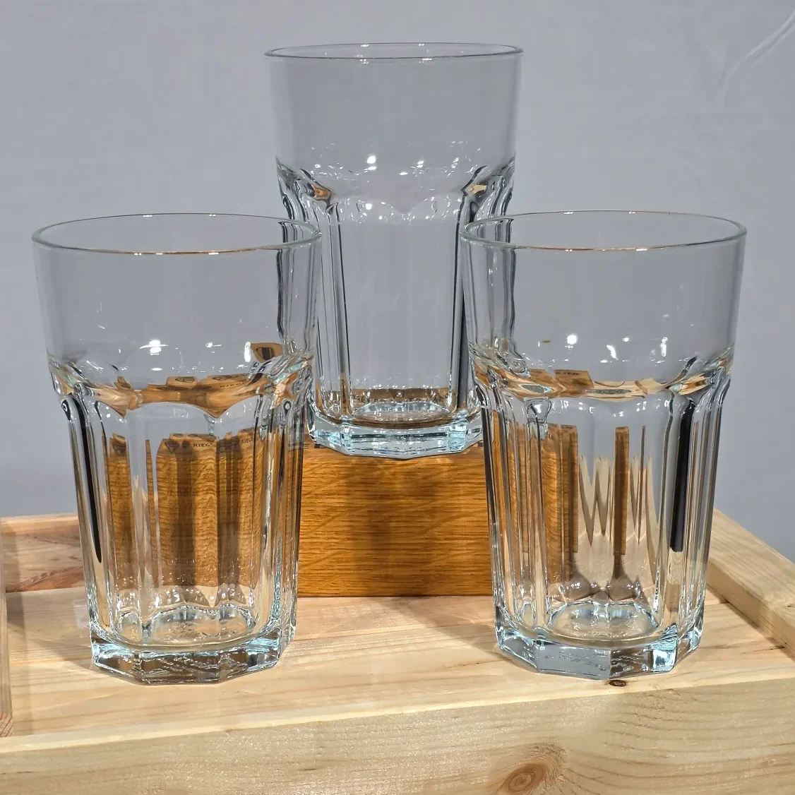 Drei klare Gläser in verschiedenen Höhen auf einem Holzuntergrund.