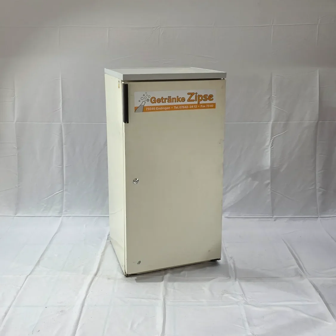 Kleiner, weißer Kühlschrank mit orangefarbenem Logo auf der Vorderseite.