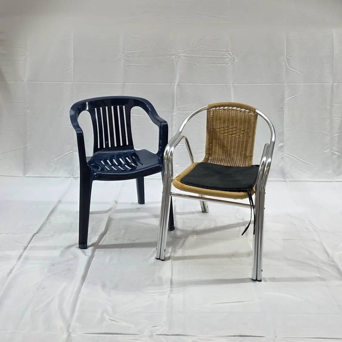 Zwei Stühle: ein blauer Kunststoffstuhl und ein metallischer Stuhl mit geflochtener Sitzfläche.