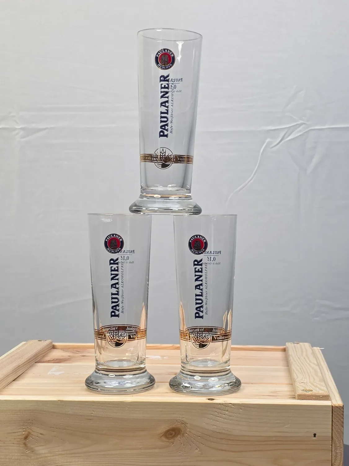 Drei kleine Trinkgläser auf einem Holzbrett mit einem Logo.
