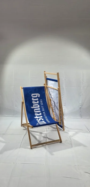 Holzliegestuhl mit blauer Stoffbespannung, vor neutralem Hintergrund.