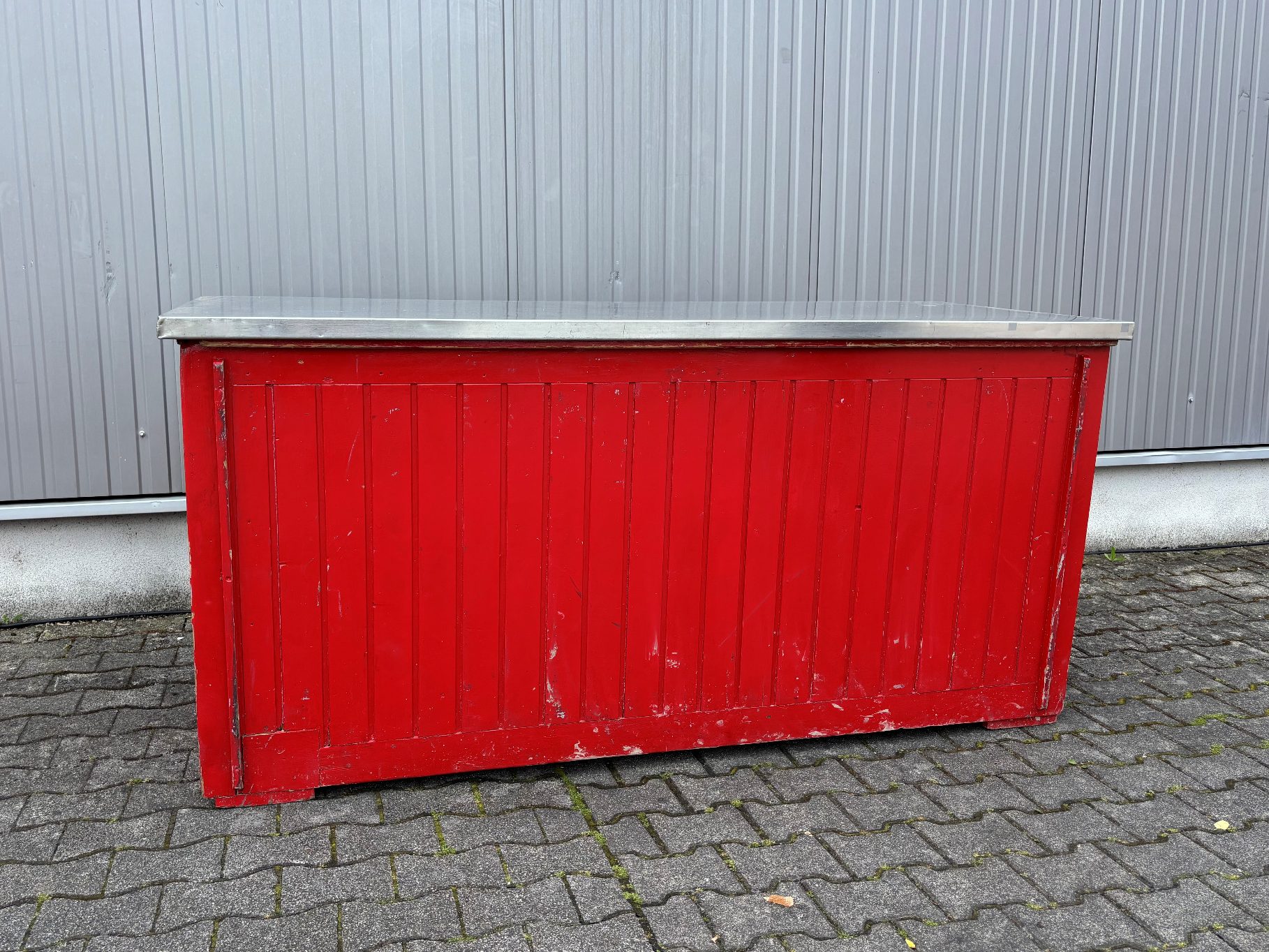 Theken in Vollfläche Rote Holztheke mit metallener Oberseite, auf grauer Steinfläche.