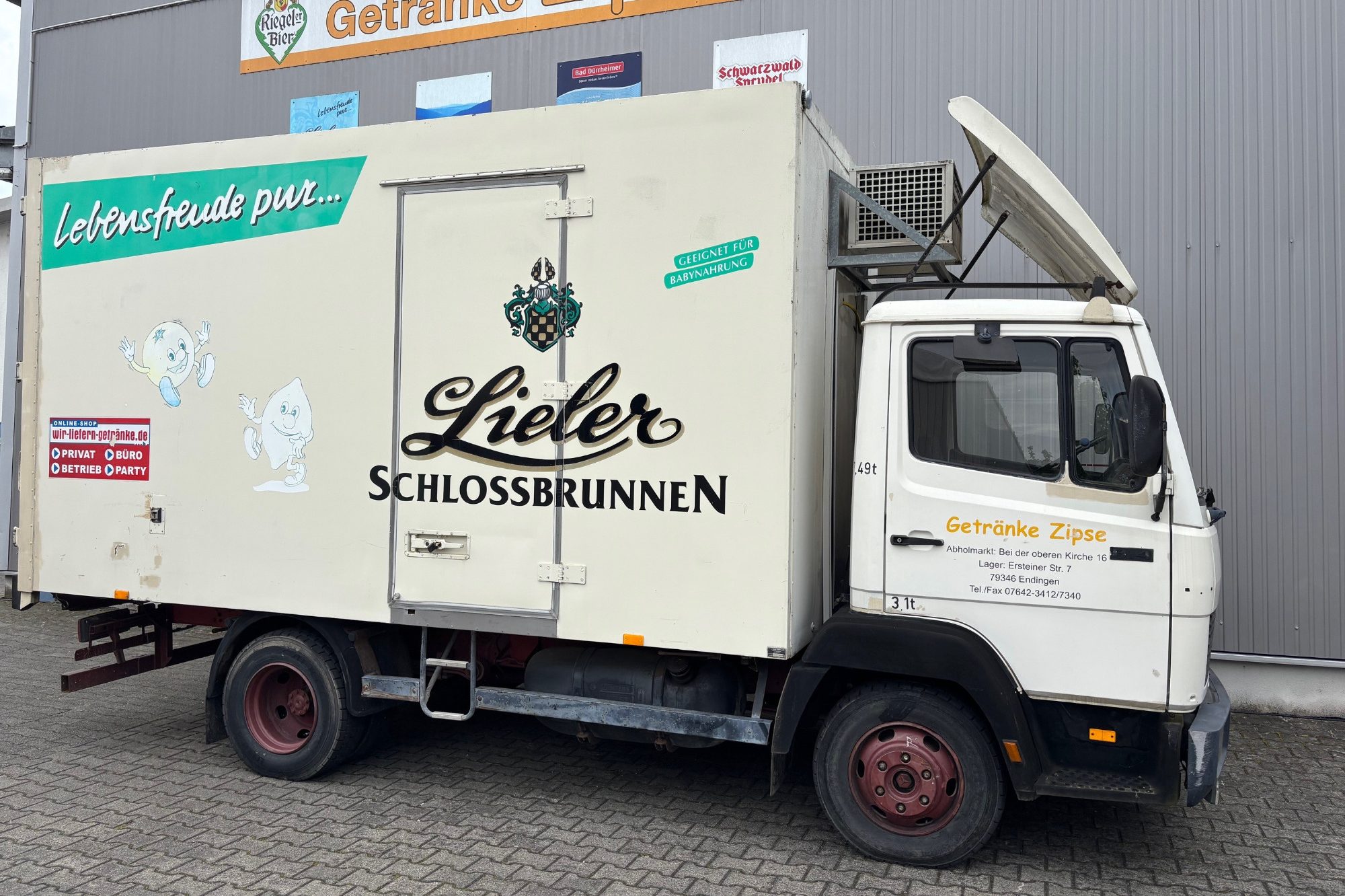 Ein geparkter Lieferwagen mit Aufschrift „Lieler Schlossbrunnen“ und geöffnetem Fahrertür.