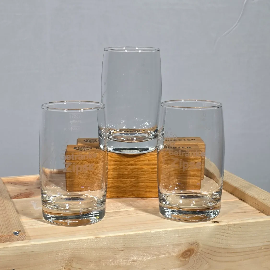 Drei leere Gläser in unterschiedlicher Höhe auf einer Holzbox.