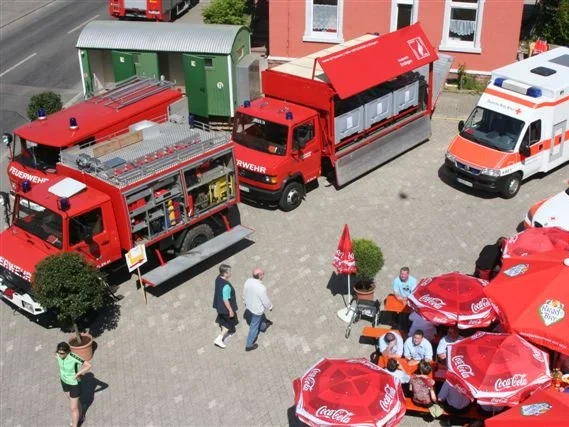 Drei Fahrzeuge, darunter ein Feuerwehr- und ein Rettungswagen, umgeben von Besuchern und Tischen.