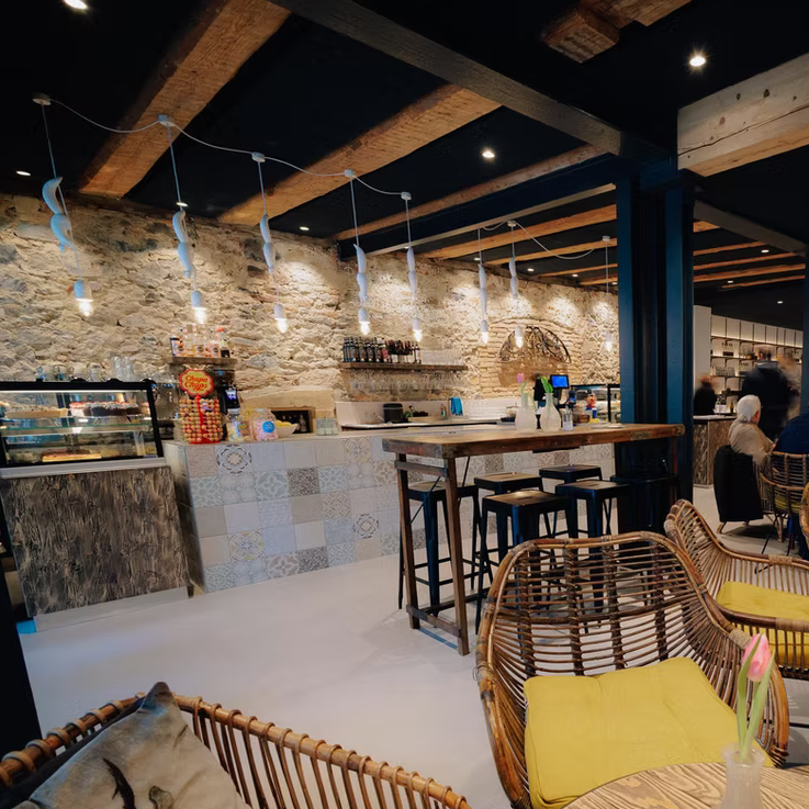 Gemütliches Café mit Steinwänden, Holzbalken und Sitzgelegenheiten aus Rattan.