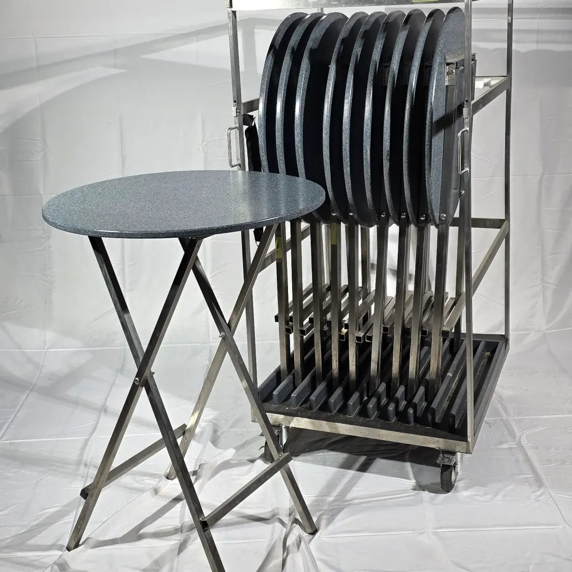 Ein Tisch und ein Gestell mit gestapelten runden Stehtischen auf Rädern.