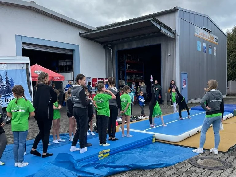 Gruppe von Menschen auf einer Sportveranstaltung mit Trainingsgeräten und Kulisse.