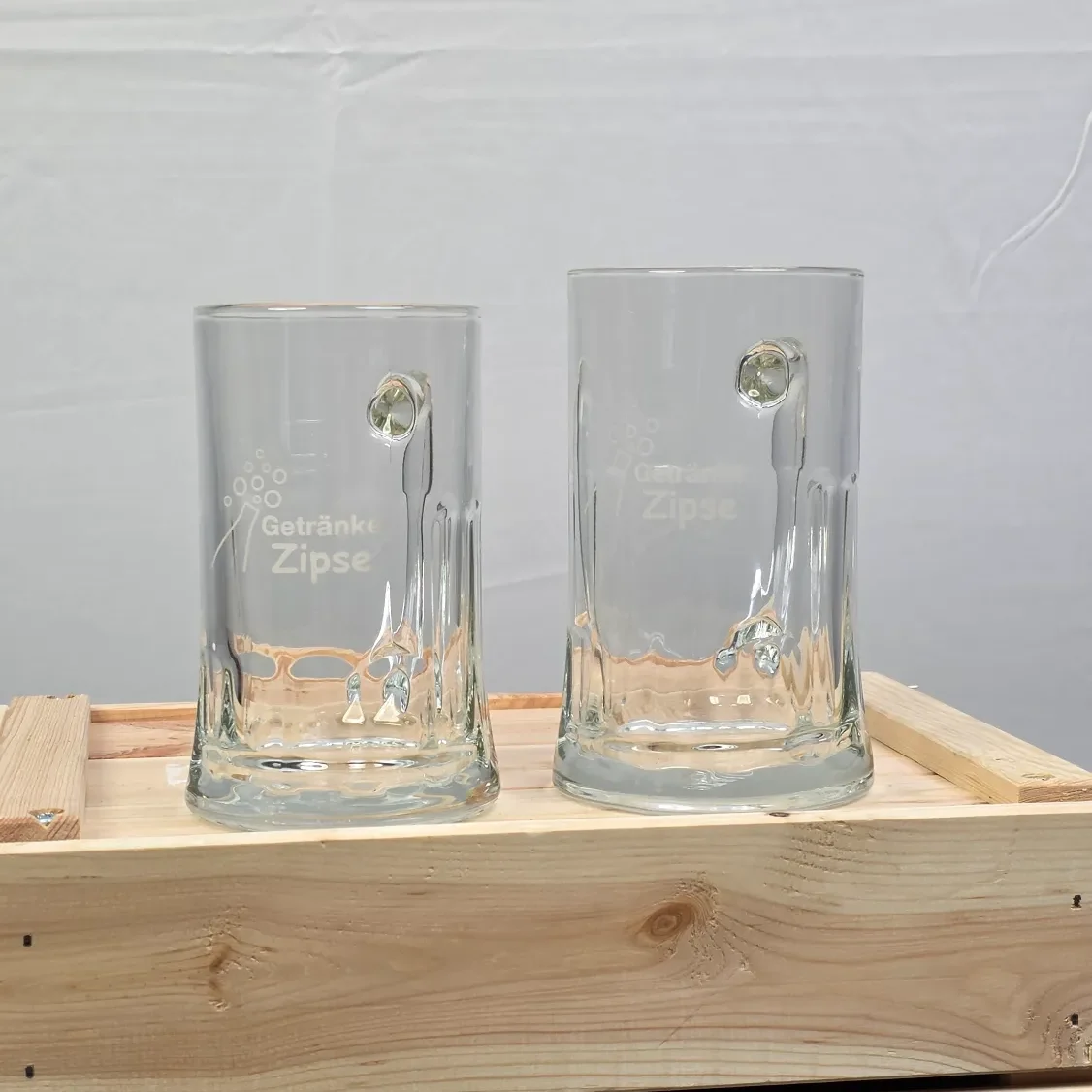 Zwei Bierkrüge aus Glas mit gravierten Designs, auf einer Holzunterlage.