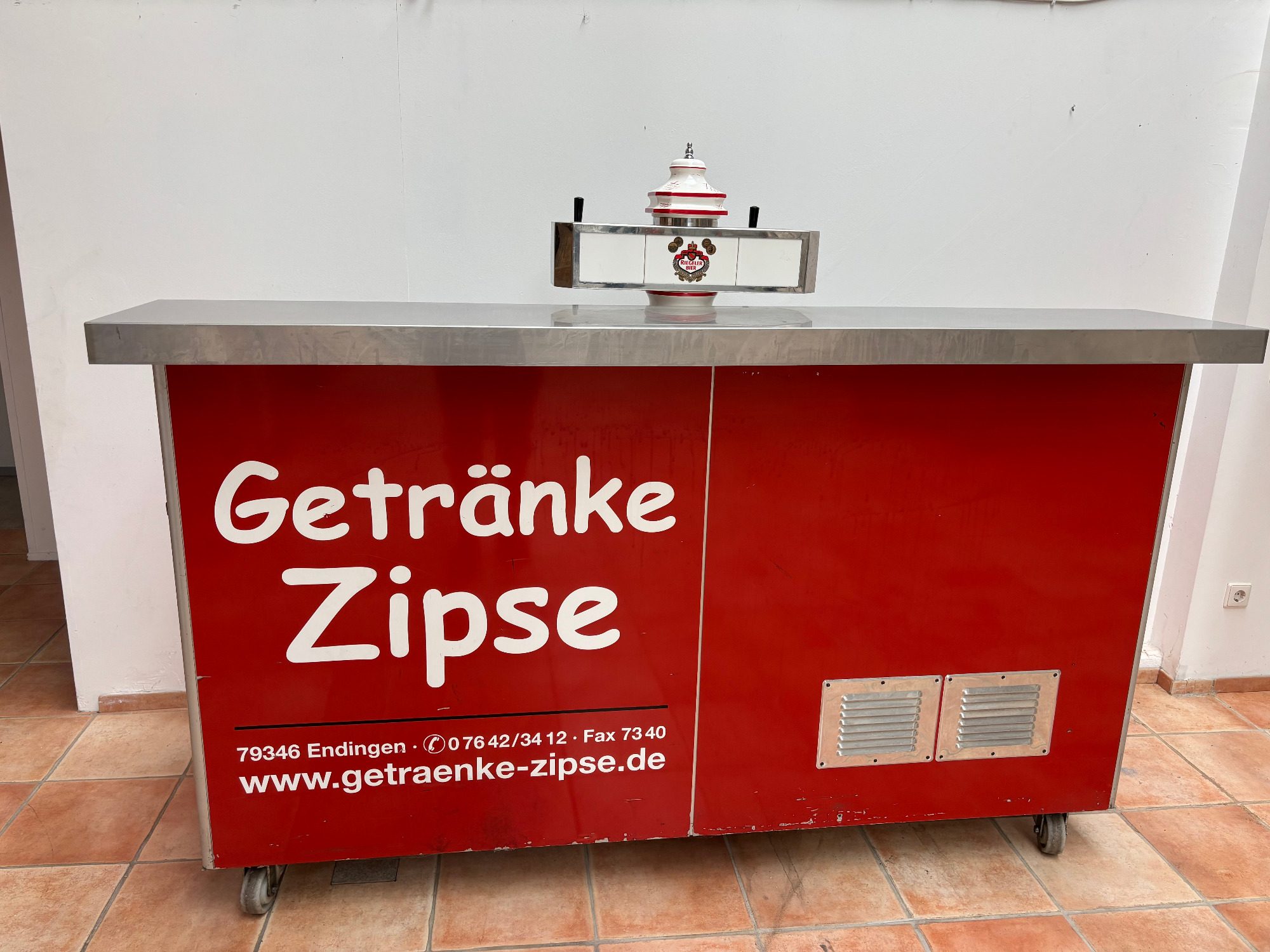 Theke 2-leitig Rote Getränkebar mit Edelstahlarbeitsfläche und Website-Adresse von Getränke Zipse.