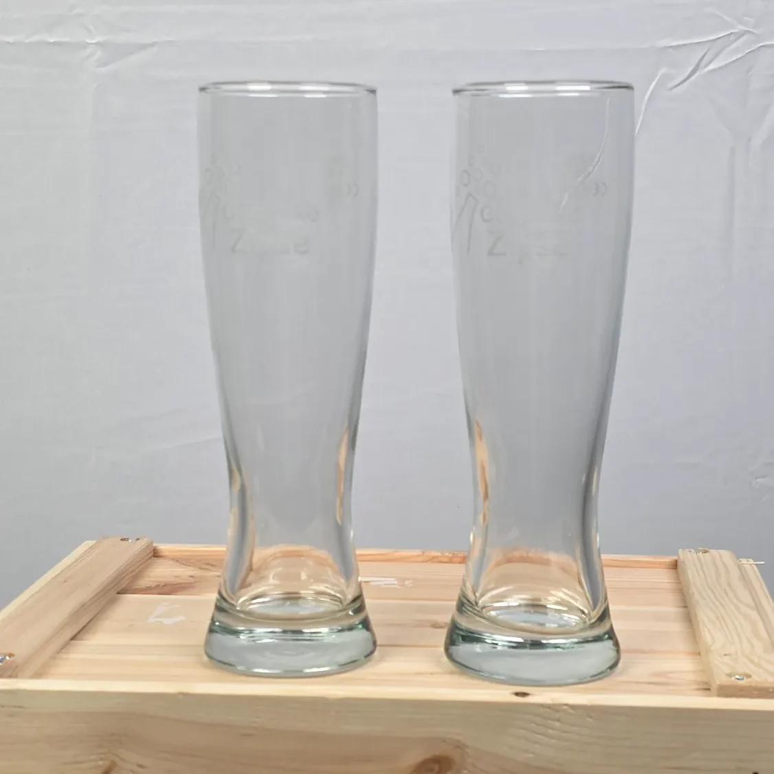 Zwei leere, hohe Weizen-Bierläser auf einer Holzbox.